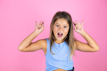 Young beautiful child girl over isolated pink background doing ok sign with fingers and smiling, excellent symbol