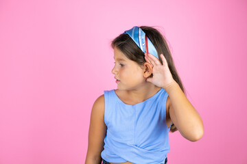 Young beautiful child girl over isolated pink background surprised with hand over ear listening an hearing to rumor or gossip