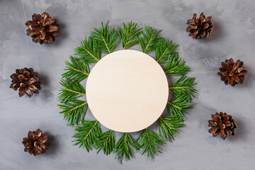 Spruce branches are laid out in form of circle, in the middle there is wooden round. Nearby is cone. New Years Christmas concept for postcard, banner. Gray background, copy space, minimalism, flat lay