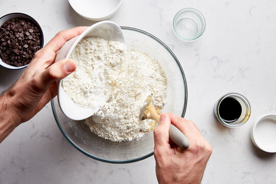 Man adding flour to dough mixture for chocolate chip cookies.