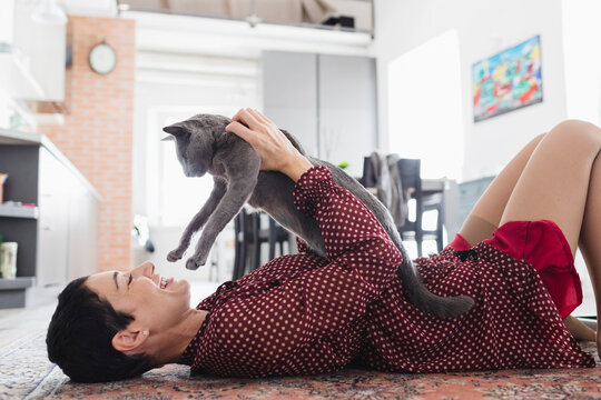 Smiling woman playing with her cat on the carpet