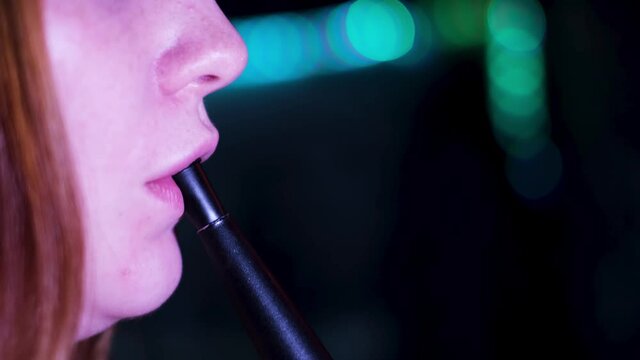 Close up of lips releasing vape smoke of e-cigarette or hookah on dark background. Media. Face details of a caucasian woman lips exhaling shisha smoke.