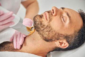 Handsome bearded man having laser hair removal procedure - obrazy, fototapety, plakaty