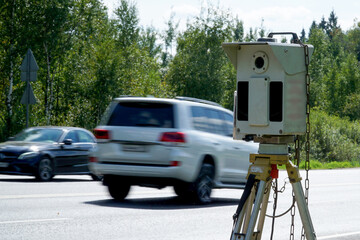        A speed control radar mounted on a tripod stands on the side of the road and controls the speed of moving cars.