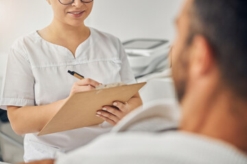 Female beautician talking with young man and taking notes