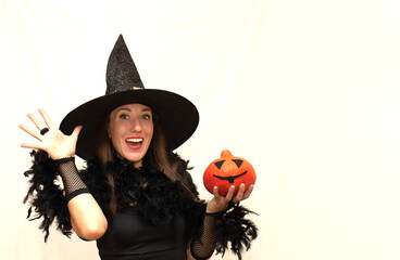Happy young woman in a Halloween witch costume holding a pumpkin on a white background. Party,...