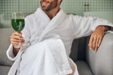 Bearded young man drinking smoothie in spa salon