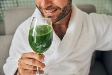 Cheerful young man with stubble drinking green smoothie