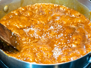 cooking salted butter caramel sauce at home kitchen - boiling melted sugar and butter and cream with added coarse sea salt in steel pan close up