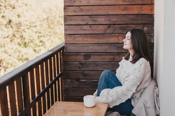 Young woman drinking tea on a balcony of a wooden house.