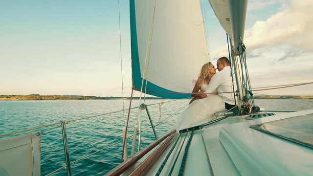 The newlyweds are sailing on the lake aboard the yacht. They enjoy each other, look and smile. Touching each other's noses