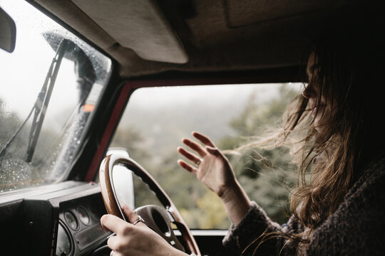 young woman driving waving hand in air