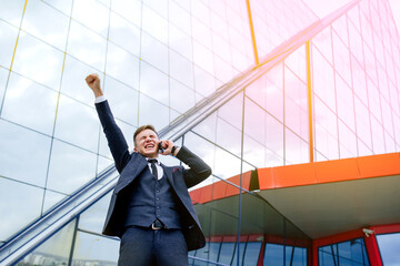 Successful Businessman Overjoyed With Phone. surpriseat at work with modern office building,...