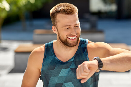 sport, technology and healthy lifestyle concept - happy smiling young man with fitness tracker in city