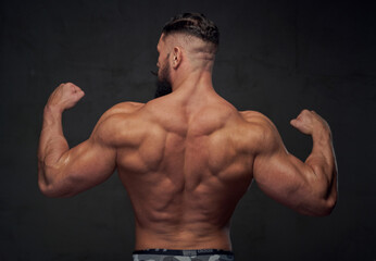 Fototapeta na wymiar Brutal bodybuilder with strong hands and with modern hairstyle posing in gray background.