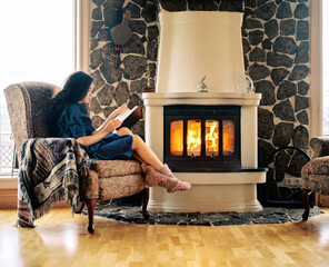 Young woman sitting by fireplace and reading