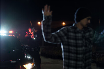 A suspect stands with raised hands as a Police Officer has his gun drawn