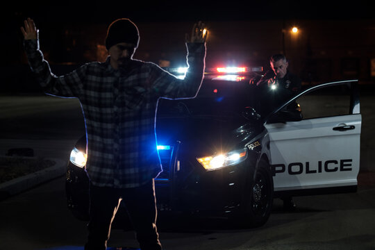 A suspect stands with raised hands as a Police Officer has his gun drawn