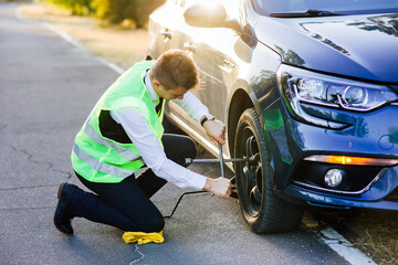 man in a green safety vest changes wheels on a car. unscrews the wheel nuts with a wrench. car service. lifts the car with a jack