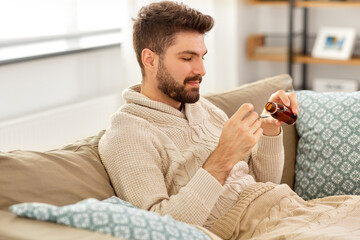 healthcare, people and medicine concept - sick man pouring antipyretic or cough syrup from bottle to spoon