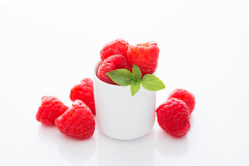 Fresh garden raspberries in a white glass on a white background, close-up