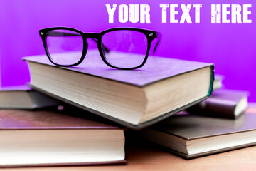 Books and eyeglasses on a wooden table, on purple soft background