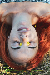 Close up portrait of red hair woman girl with freckles. Portrait of a girl outdoors in sunlight. Portrait upside down, yellow flowers in her hair. Closed eyes