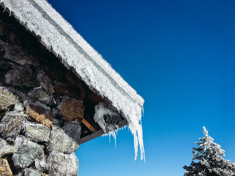 Large Icicles Hanging From Roof With Blue Sky