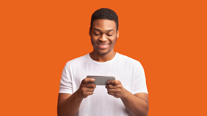 Interested afro guy using smartphone over orange background