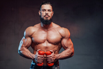 Fototapeta na wymiar Brutal and muscular guy with beard and with red dumbells posing in gradient studio background.