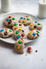 American cookies with chocolate chips and colored sweets, bottles with milk and straws on a gray background