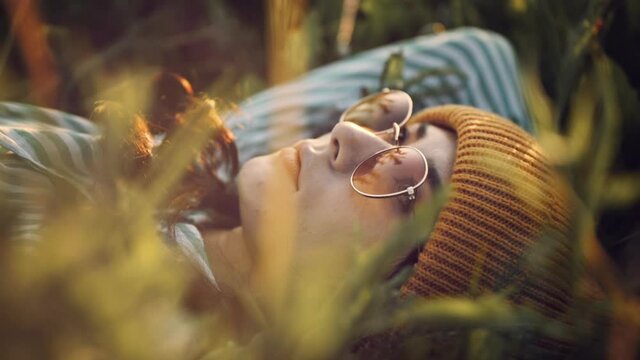 Social distancing and solo activity. Beautiful young girl on self isolation laying on the sunset field enjoying her loneliness. Portrait of hipster japanese in stylish sunglasses and yellow cap.