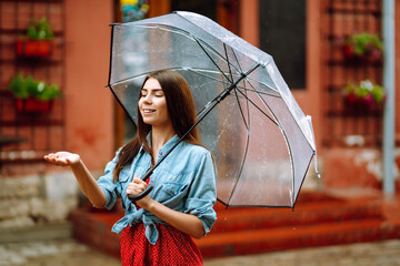 Cheerful woman holding umbrella while strolling outside. Beautiful woman with umbrella on a rainy...