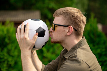 Handsome male football fan kisses soccer ball, Happy young man support sport team, celebrating...