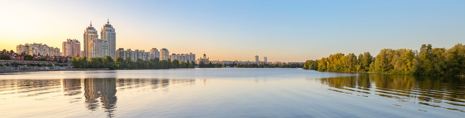 Fototapeta na wymiar Panoramic view oth the high Obolon buildings near the Dnieper river in Kiev, Ukraine. Blue clear sky and reflection in the water.