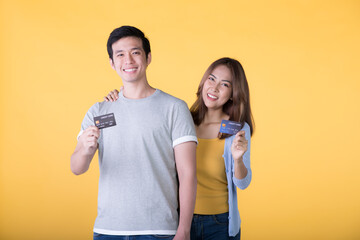 Young Asian couple showing credit cards isolated on yellow background