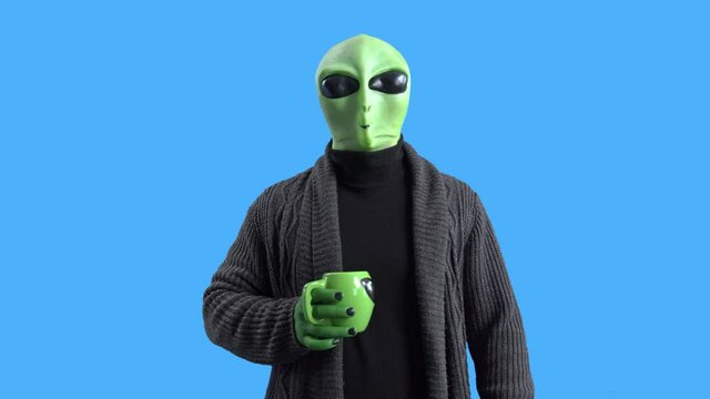 Alien in a stylish black cardigan walks around the spaceship with a mug of hot drink, walks and looks around, drinks coffee. Chromakey. Morning routine.