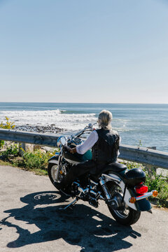 Aged Woman relaxing by the Coast on Her Motorcycle