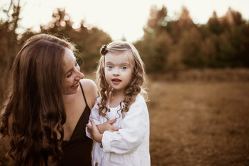 Fototapeta premium Charming young Caucasian mom and daughter blonde with long hair in a field in summer, lifestyle and brown toning. Candid childhood and motherhood
