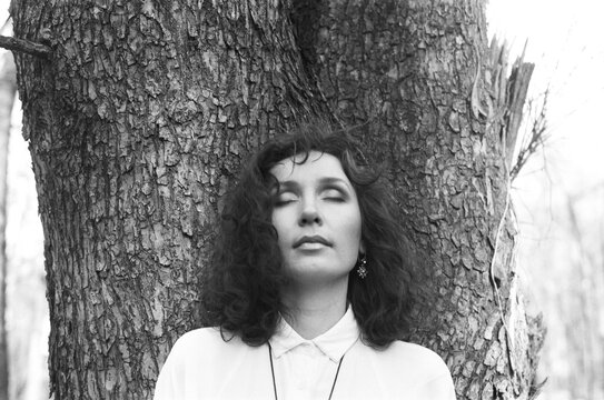 A portrait of a beautiful woman nearby tree with a closed eyes