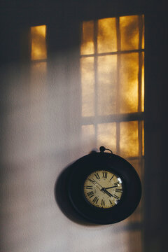 Clock and sunrays on wall indoors at sunset