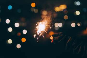 Woman holding sparkler against city lights