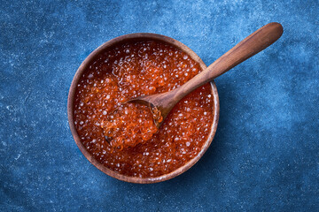 Red caviar in a wooden bowl and spoon with caviar on blue background. Top view, copy space