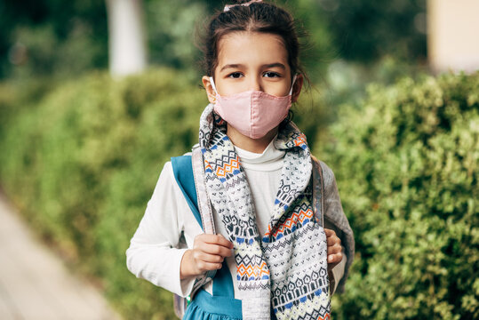 Outdoor Horizontal Image Of Cute Child Wearing Protective Face Mask Going Back To The School During Coronavirus. Smiling Little Girl Student With Backpack Looking To The Camera Posing Outside.