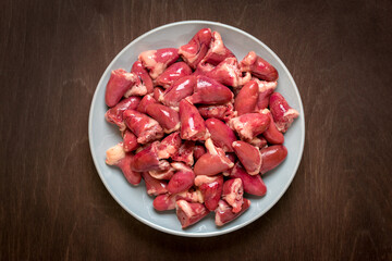 Raw fresh chicken hearts in gray plate isolated on wooden background top view Flat lay Offal ready for cooking Healthy food