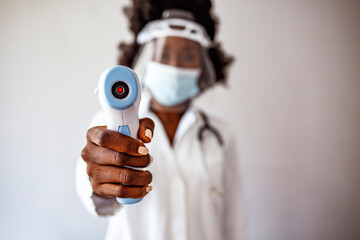 Close-up shot of doctor wearing protective surgical mask ready to use infrared forehead thermometer...