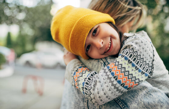 Outdoor image of happy little girl in yellow cap hugging her mom. Cute kid embracing her mother enjoying the time together outside. Mother and daughter share love. Mother's day.