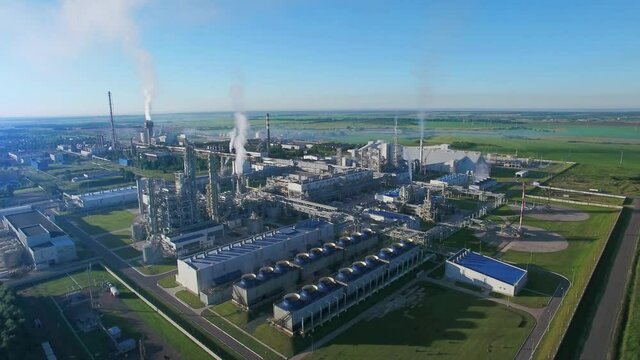 Chemical Plant produces gasoline and mineral fertilisers. Aerial flying morning sunshine summer fields and grass around. Smoke smog and environmental pollution.
