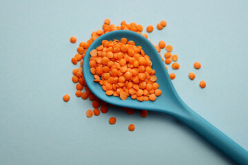 Red lentils in a blue bamboo spoon on a light blue background.
