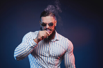 Obraz premium Elegance and bearded bodybuilder in fashion of mafia member smoking cigar and posing in dark background.
